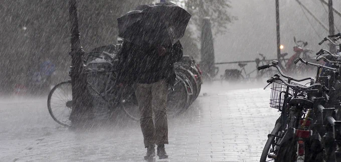 Picture shows a person walking in a rainstorm with an umbrella. 
