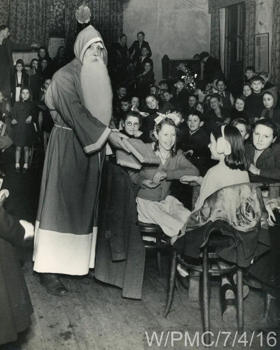 A black and white photograph of Father Christmas giving presents to children at a party (ref. W/PMC/7/4/16).