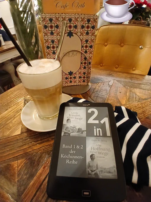 EBook auf einer Tischplatte. Daneben ein Latte Macchiato und ein Ständer mit Speisekarten. Dahinter Blick in ein Café. 
Band 1&2der Köchinnen Reihe von Petra Durst-Benning