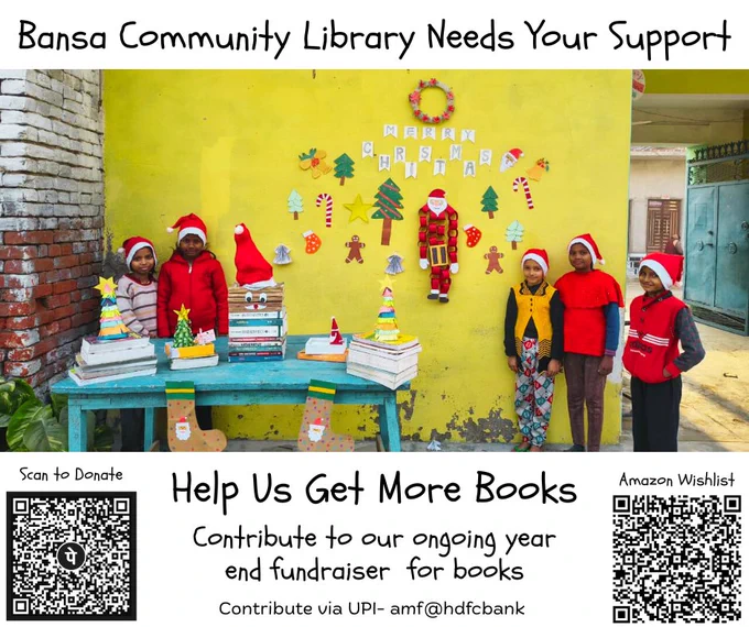 A group of children wearing red winter clothes and Santa hats stand outside the Bansa Community Library against a bright yellow wall decorated with handmade Christmas crafts, a wreath, and a “Merry Christmas” banner. A blue table in front displays stacks of books and festive paper decorations. Text on the poster reads: “Bansa Community Library Needs Your Support” and “Help Us Get More Books.” At the bottom are two QR codes labeled “Scan to Donate” and “Amazon Wishlist,” along with text inviting contributions to the year-end fundraiser and a UPI donation option (amf@hdfcbank).