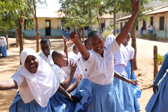 Excited students in uniforms waving and smiling in a schoolyard.