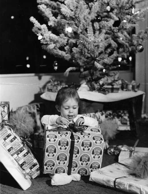 A child opening a gift in front of a Christmas  Tree.