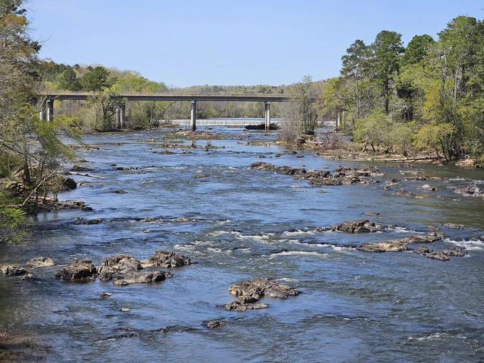 A river with some rocks and rapids and a bridge in the background.