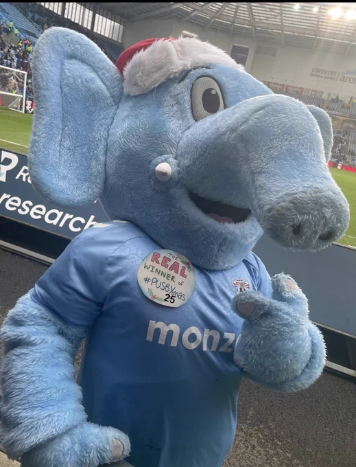 Sky blue sam pointing at a winner of pusbxmas 25 badge