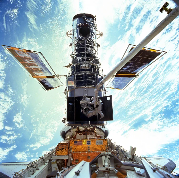An astronaut conducts a spacewalk on the Hubble Space Telescope, which is orbiting above the Earth's surface.
