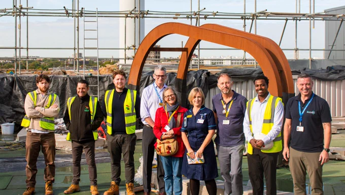 Group of construction and healthcare workers standing together on a rooftop with scaffolding and industrial structures in the background.
