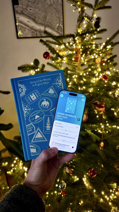 Me holding the cloth bound edition of Around the World in 80 days in my hand together with an iPhone running PocketShelf. The book cover is blue and shoes illustrated stamps from locations like Singapore, Bombay, Egypt, Paris etc.