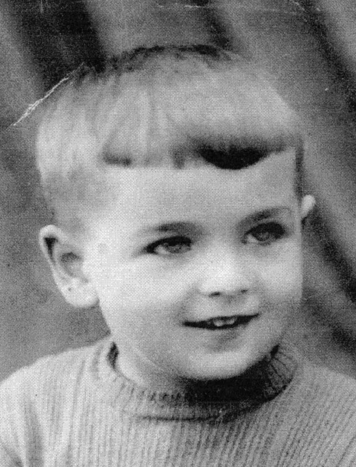 An ID photo of a young boy in a sweater. He has short hair. He is looking to the right and gently smiles. 