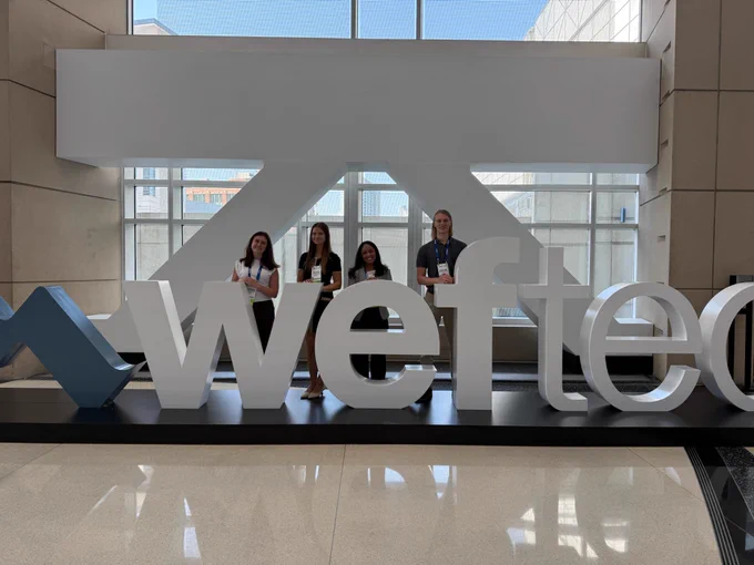 The student team smiles at the camera behind a sign for the competition.