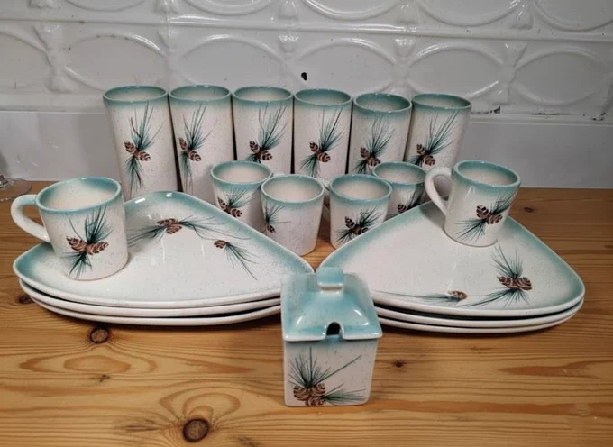 A 19-piece collection of vintage Romco Rocky Mountain pottery featuring a matte teal ombre glaze and speckled cream base. The set includes 6 triangular snack plates, 6 matching coffee mugs, 6 tall tumblers, and a square covered sugar bowl, all decorated with a hand-painted pinecone and needle motif."