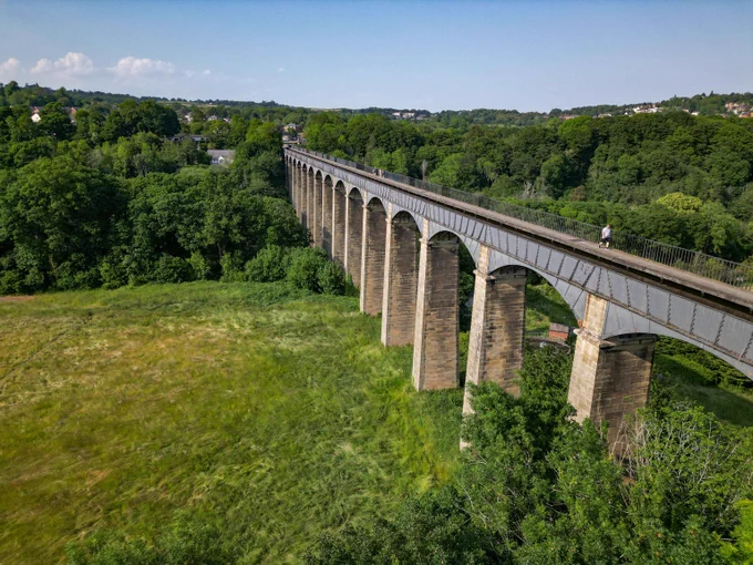 Pontcysyllte Aqueducts' grand stone and iron structure spans across a green landscape with a blue sky. 