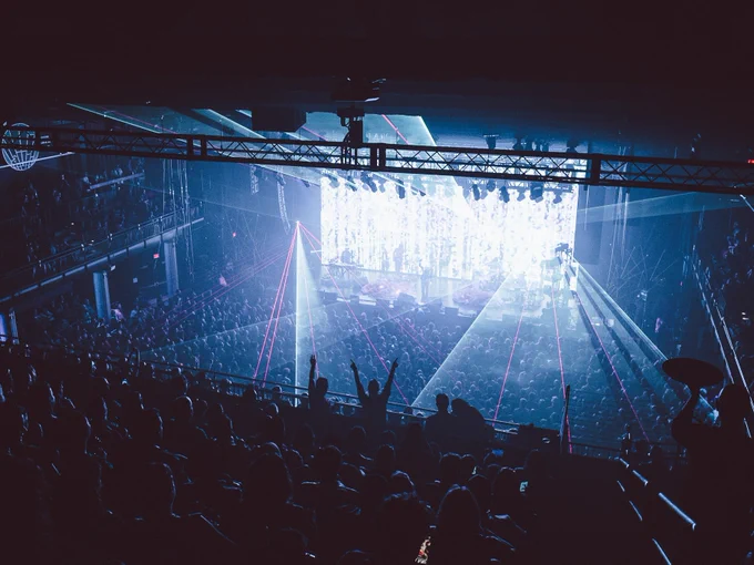 A concert scene at GLC Live at 20 Monroe with a crowd watching a vibrant stage illuminated by blue lights and laser beams.