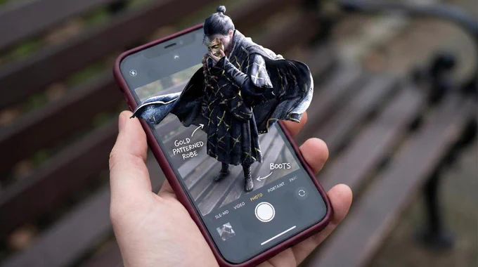 ​A hyper-realistic optical illusion composite photo. A hand holds a smartphone with a burgundy case displaying the iOS camera interface. The character Jiang Wulang from the game Where Winds Meet is on the screen, but his upper body, wearing traditional Wuxia robes and holding a golden mask, physically extends out of the top of the phone into the real world, creating a 3D pop-out effect. Background is a blurred park bench.
