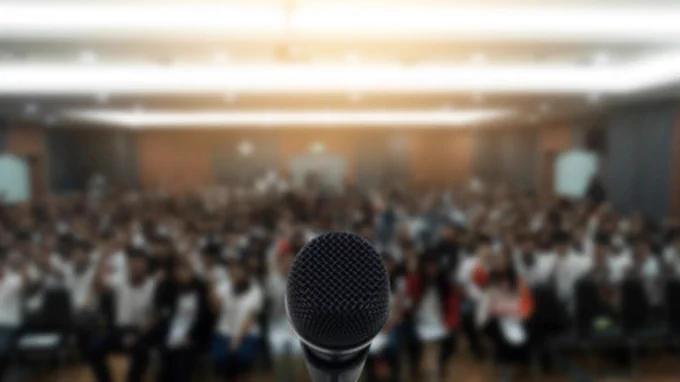 Close-up of a microphone with a blurred background of an audience in a conference hall.