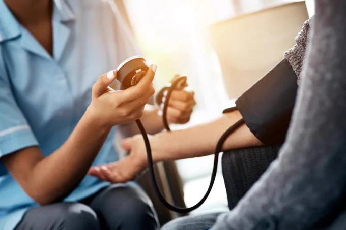Healthcare professional using a blood pressure cuff on a patient's arm during a medical check-up.