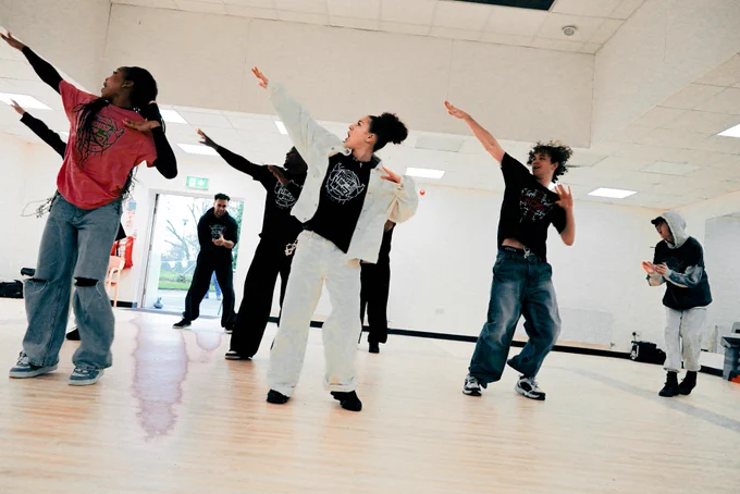 A group of individuals from House of Wingz practicing dance moves in a studio, wearing casual clothing.