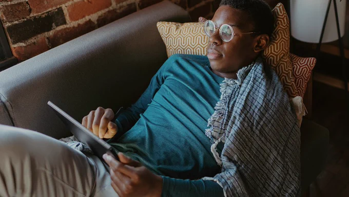 A person is lying on a couch and using a tablet.