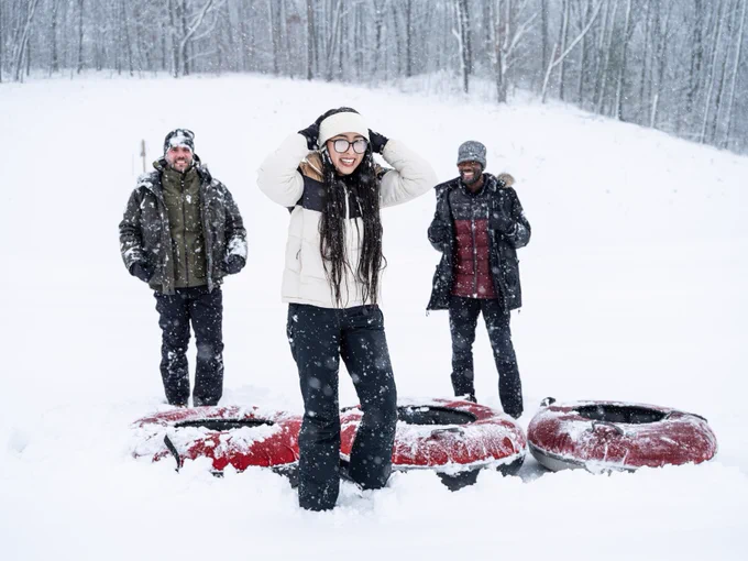 Three people are standing in a snowy landscape with colorful snow tubes, smiling and enjoying the winter weather.