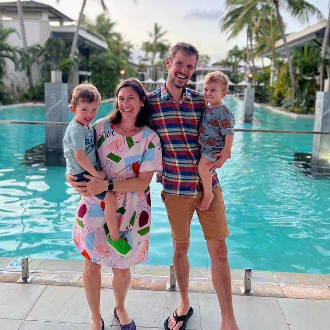 a picture of a family of 4, smiling to camera on holiday in front of a pool and palm trees