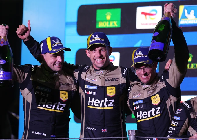 Standing shoulder to shoulder on the podium, Cadillac team-mates Earl Bamber, Jenson Button and Sébastien Bourdais raise their arms in celebration. All are wearing black and gold, Hertz branded race suits. 2025 WEC São Paulo.