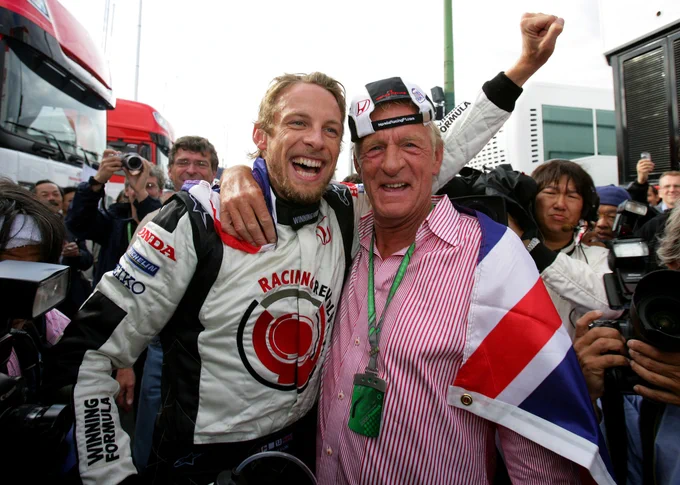 Fist in the air and crowded by the press, a jubilant Jenson Button stands shoulder to shoulder with father John, who wears a pink shirt, Union flag over his back and a backwards BAR Honda baseball cap. 2006 Hungarian Grand Prix.