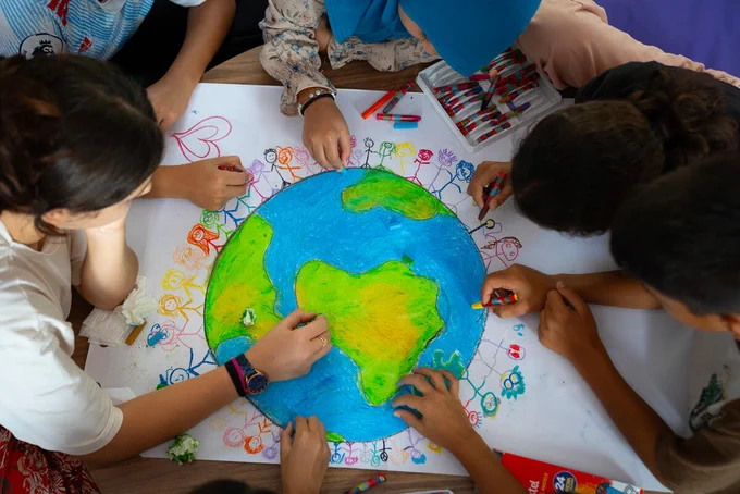 Kinder sitzen im Kreis und malen gemeinsam die Erdkugel in bunten Farben.