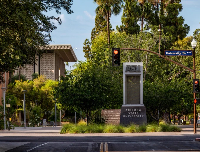 Arizona State University on University Drive surrounded by greenery and palm trees under a clear sky.