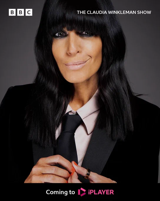 A woman in a black suit and tie smiles to camera, playing with her hands