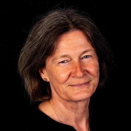 Fiona Donald smiles for a headshot against a black background. She has black hair, green eyes and white skin.