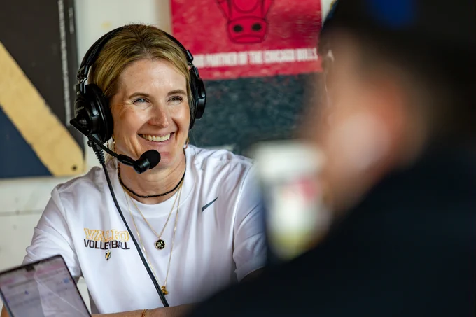 Valpo Volleyball Coach Carin Avery smiles while wearing radio recording equipment.