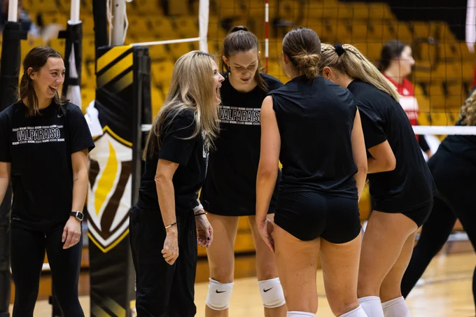 Valpo Volleyball Coach Carin Avery celebrates with players at the net during a match.