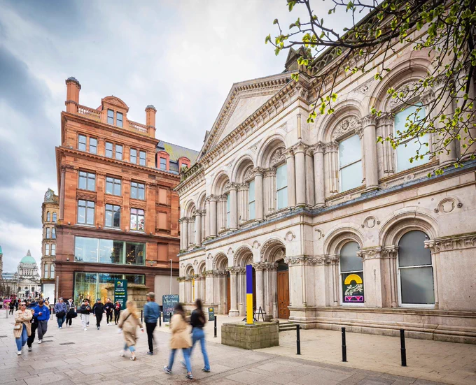2 Royal Avenue - an historic stone building with arched windows, in the city centre beside another building and fronting on to a busy pavement area.