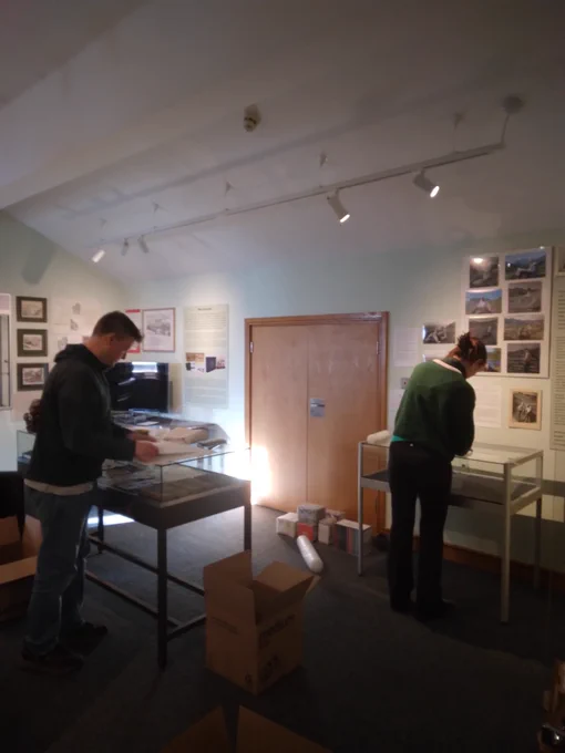 Two individuals deinstalling an exhibition in a museum space, organising materials and displays.