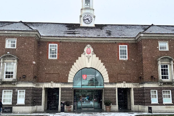 Front entrance of Middlesex University's historic brick building with a clock tower, lightly covered in snow.