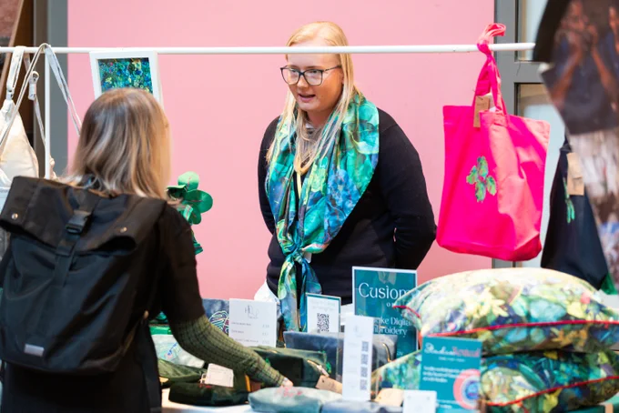 Customer browsing colorful cushions and accessories at a vibrant market stall with a pink backdrop.