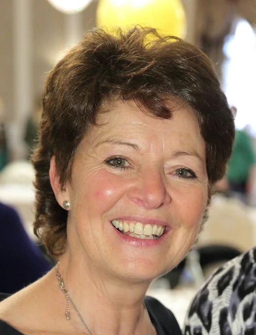 Woman with short brown hair wearing a silver necklace and small earrings at an indoor event.