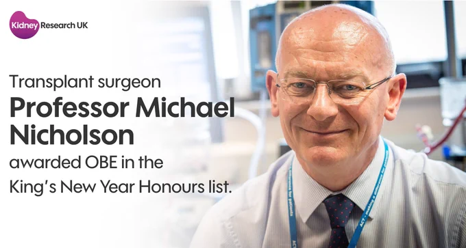 Professor Michael Nicholson, a bald, male, transplant surgeon, smiling in a lab with a Kidney Research UK banner, celebrating an OBE award in the King's New Year Honours list.
