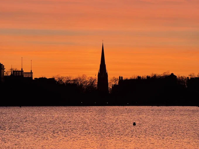 The sky turning multiple shades of red over Kensington Church and the Round Pond.