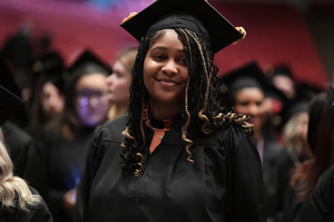 A graduate wearing a cap and gown smiles proudly during a commencement ceremony.