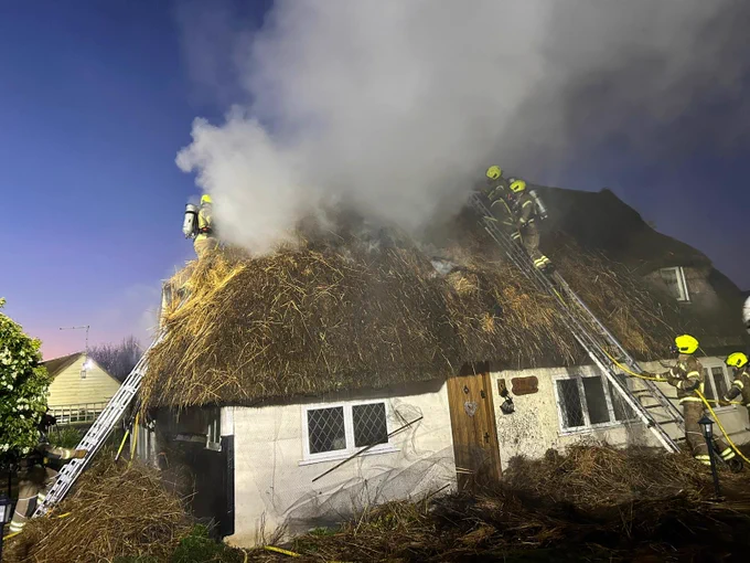 Firefighters on the smoking roof of a thatched cottage