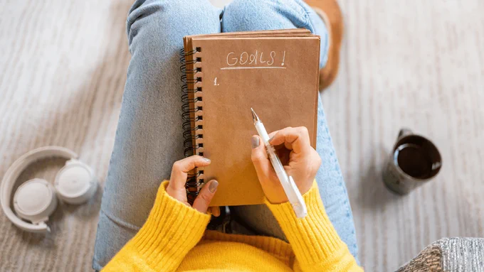 A professional writing goals in a notebook, representing meaningful and achievable work goal setting for the new year.