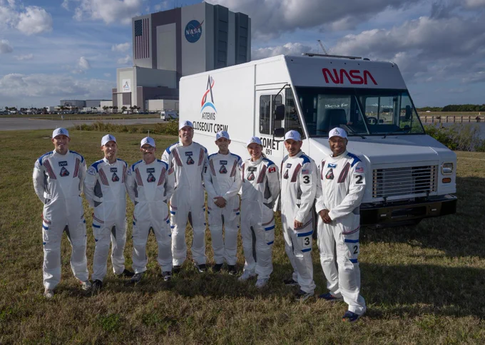 Members of the Artemis II closeout crew, from left: William Sattler; Tyler Sutherland; Michael Heinemann; Christian Warriner; Taylor Hose; Jenni Gibbons, Artemis II backup crew member; Bill Owens; and Andre Douglas, Artemis II backup crew member, pose for a photo with NASA’s Vehicle Assembly Building behind them at the agency’s Kennedy Space Center in Florida on Thursday, Dec. 19, 2025. All eight team members stand in front of a truck that is labeled “Artemis Closeout Crew.” Fluffy white clouds cover a blue sky in the background. Credit: NASA/Jim Ross