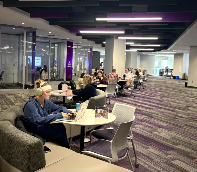 Students studying and socializing in a modern university lounge area with tables, chairs, and sofas.