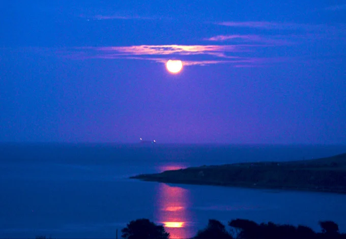 The “full Sturgeon Moon” rises over a flat-calm Courtmacsherry Bay in West Cork , Ireland as the ‘Artemis’ (container ship..) begins to pass beneath the rising moon after sunset!