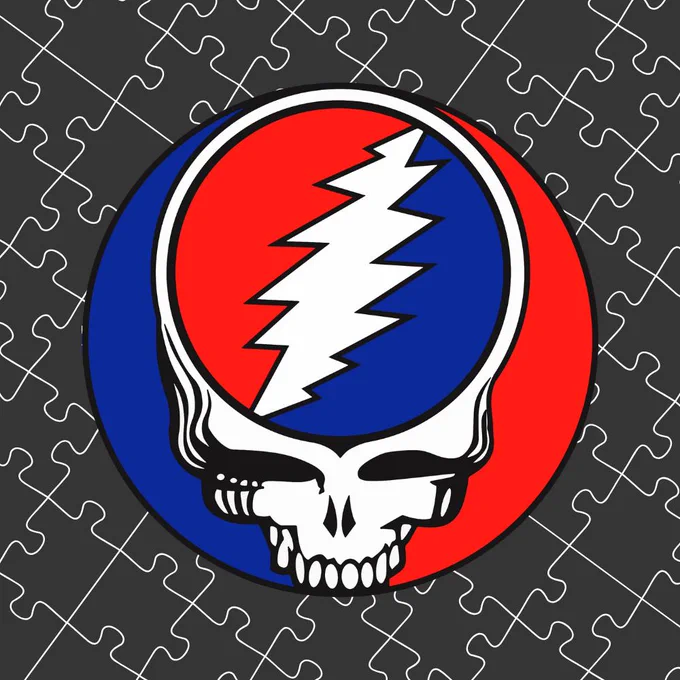 The logo for the band The Grateful Dead on a jigsaw puzzle pattern background. The logo is a red and blue circle with a white skull, and within the skull is another red and blue circle with a white lightning bolt across the middle.