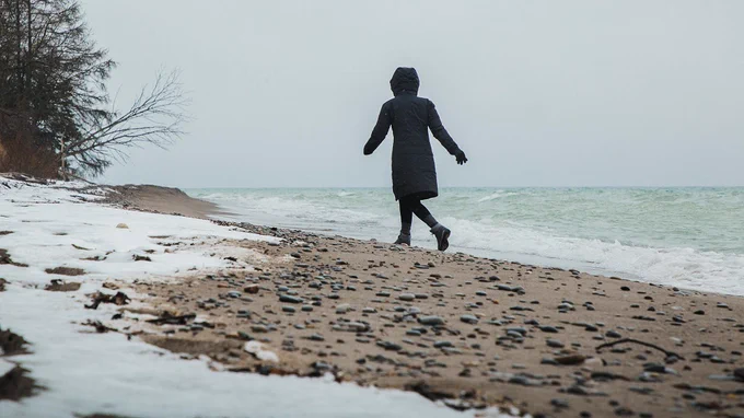 Person walking along a snowy beach beside a lake.