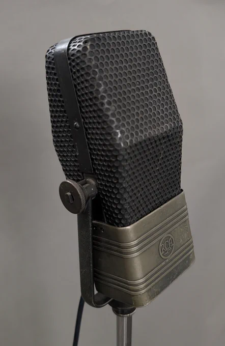Close-up of a vintage circa 1938 RCA ribbon microphone with a honeycomb grille and metal base on a stand against a gray background.