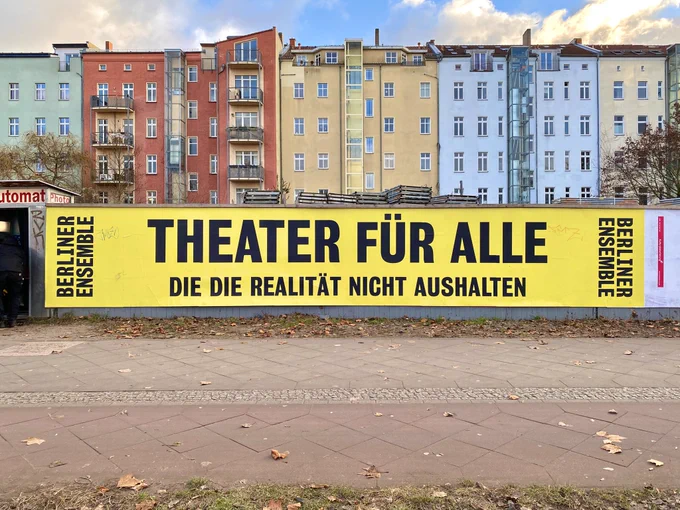 Plakatwand mit grossem gelben Banner des Berliner Ensembles mit der Schrift "Theater für alle, die die Realität nicht aushalten"