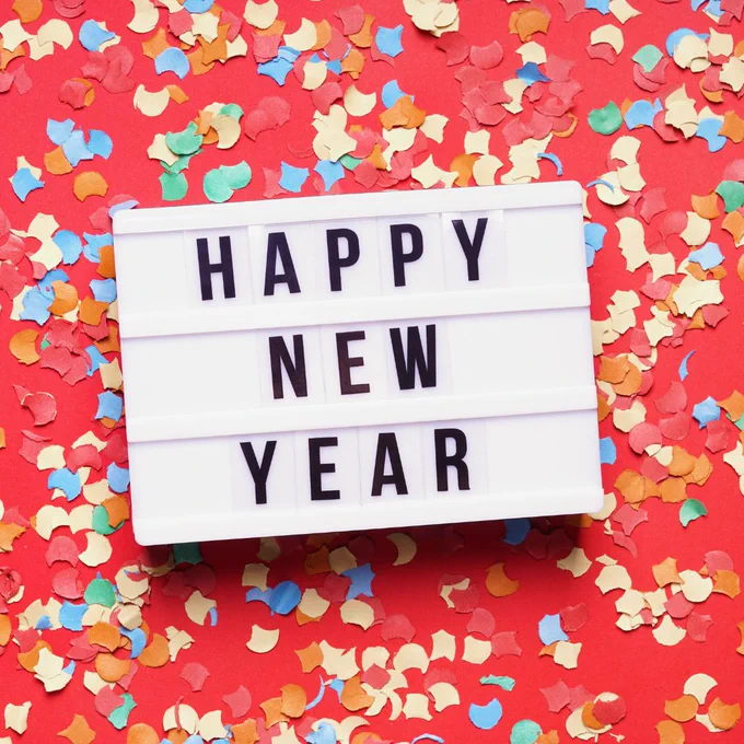A lightbox has the words happy new Year and there is paper confetti around it