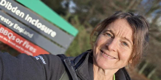 New Forest NPA ranger smiling in front of a sign for Dibden Inclosure in New Forest, England, indicating barbecues and fires are prohibited